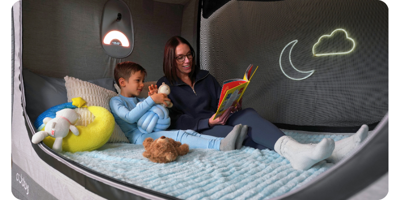 Mom reading a book to her son inside a Cubby Bed with calming lights